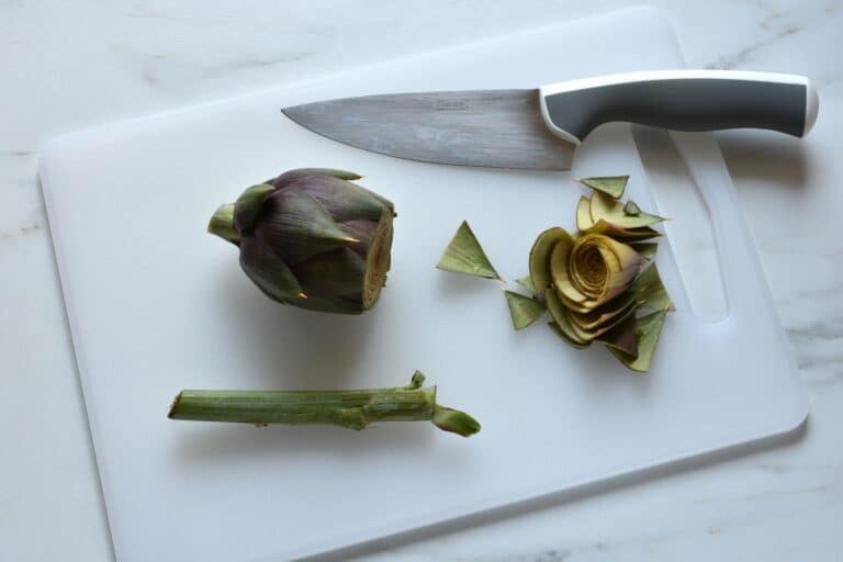 Trimming an artichoke on a chopping board with a knife.