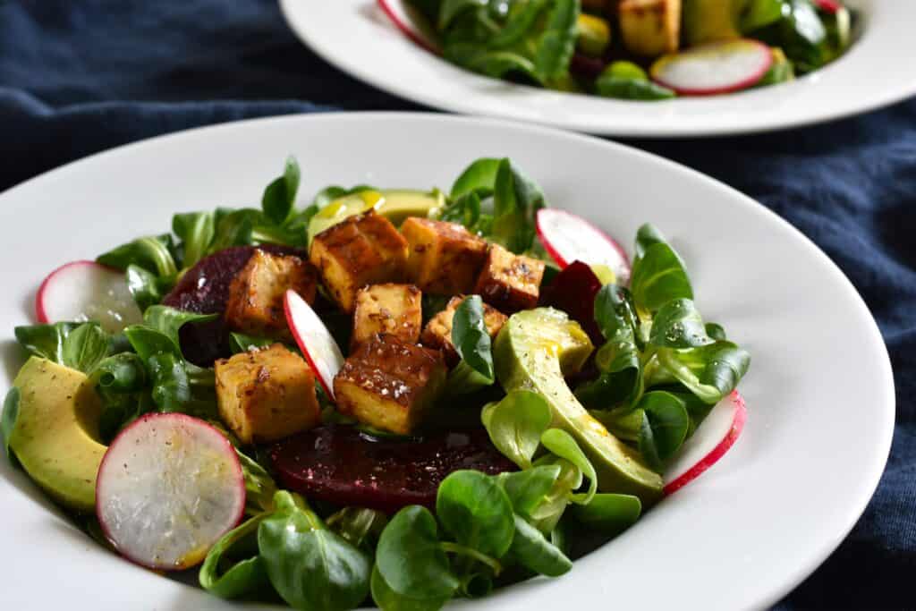 Two plates of lamb's lettuce salad with smoked tofu beetroot and avocado.