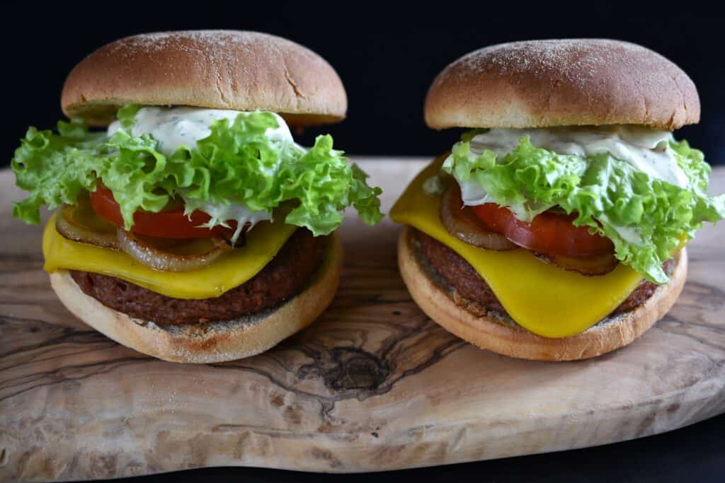 Two plant-based cheeseburgers on a wooden board.