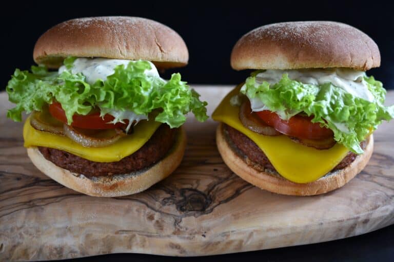 Two vegan cheeseburgers on a wooden board.