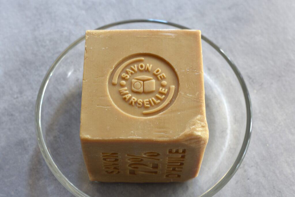 A 600 g block of pure Marseille soap in a glass dish on a worktop.