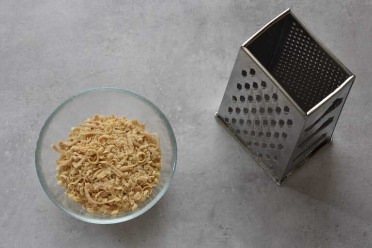 Grated Marseille soap in a glass bowl with a box grater on a worktop.