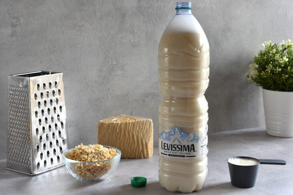 Homemade vegan laundry soap in a bottle with a box grater, grated soap, a scoop and a block of vegan marseille soap.