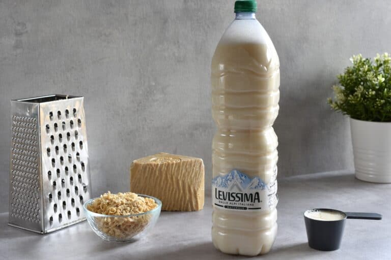 Homemade liquid laundry soap in a bottle with a lid, a box grater, grated soap, a scoop, and a block of Marseille soap.