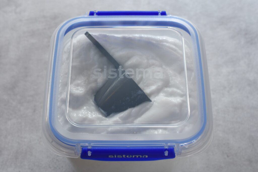 Homemade laundry soap in a plastic container with a lid.