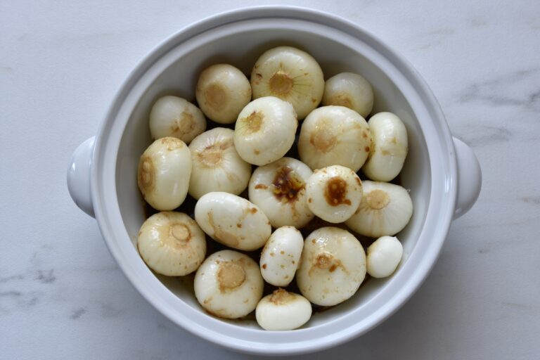 Raw borettane onions in an oven dish with olive oil and balsamic vinegar.