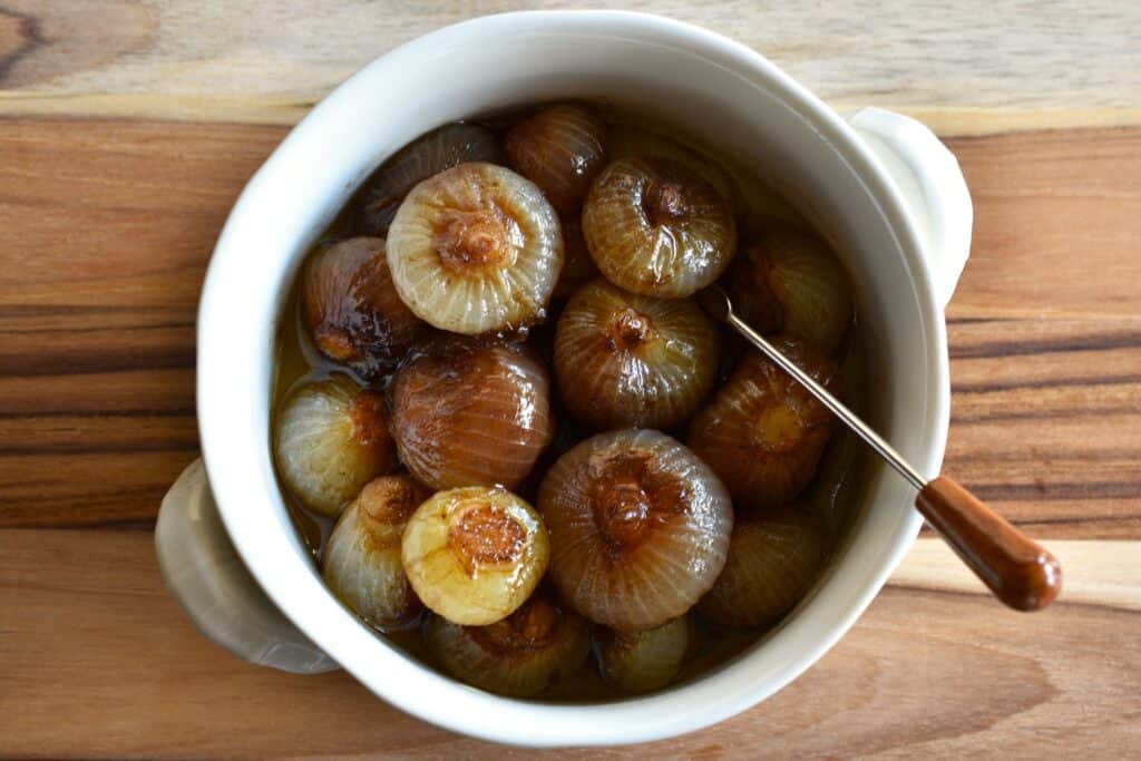 Roasted balsamic onions in a white bowl with a cocktail fork.