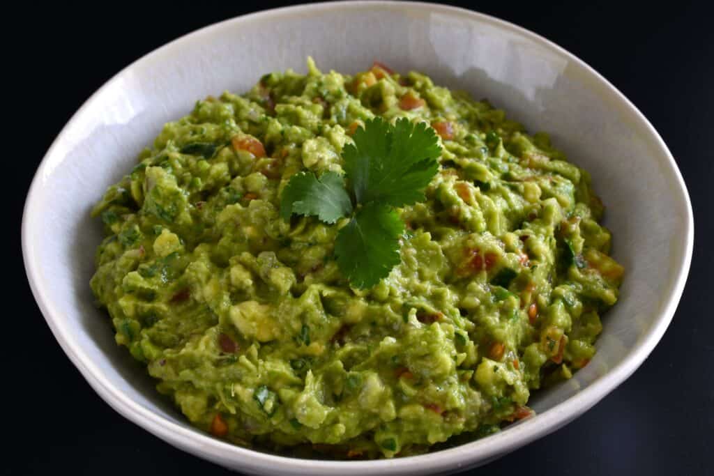 Vegan guacamole in a white bowl with a garnish of coriander leaf.