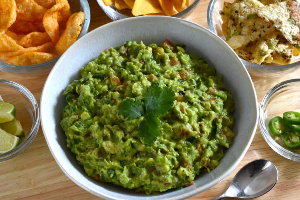 Vegan guacamole in a white bowl with tortilla chips, lime segments, and sliced green jalapeños (featured image).