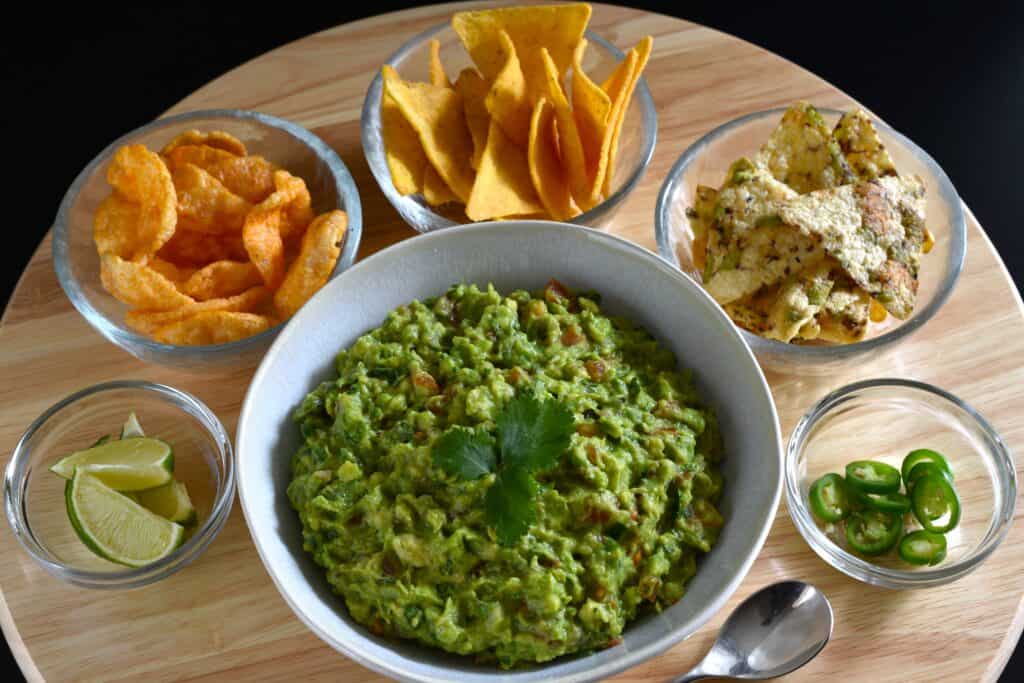 Vegan guacamole in a white bowl with tortilla chips, lime slices and sliced green jalapeño.