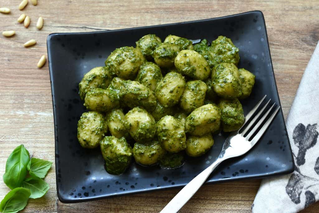 Homemade vegan potato gnocchi with basil pesto on a black plate.