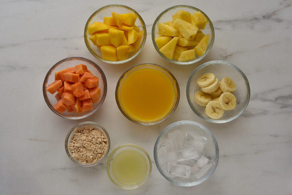 Ingredients for mango pineapple protein smoothie in individual glasses on a worktop.