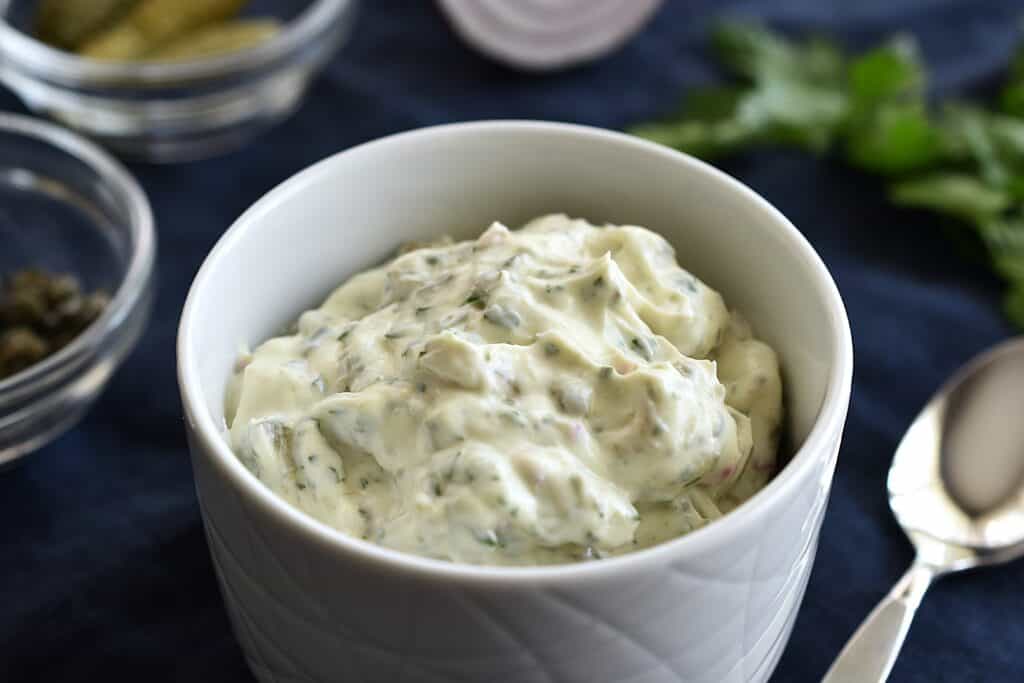 A close-up image of homemade vegan tartare sauce in a white bowl with a spoon.