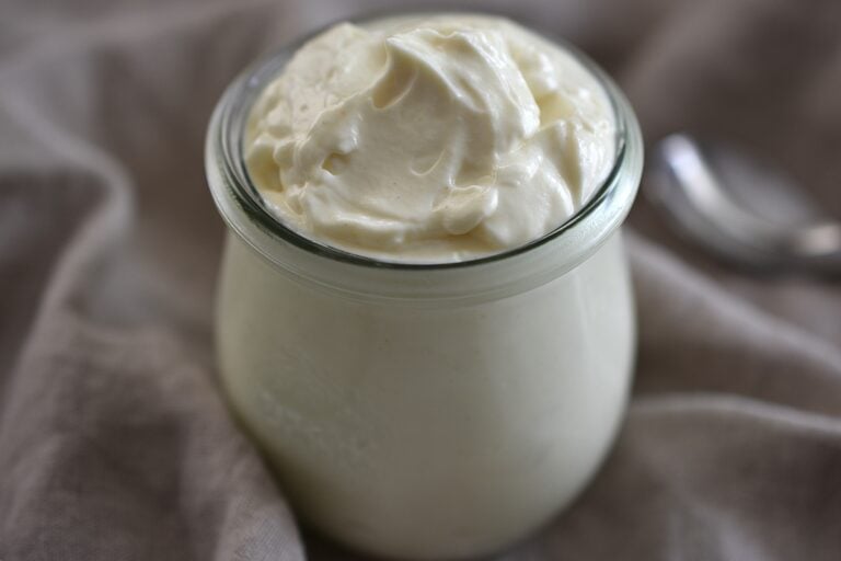 A close-up image vegan mayonnaise in a weck glass on a kitchen towel with a spoon.