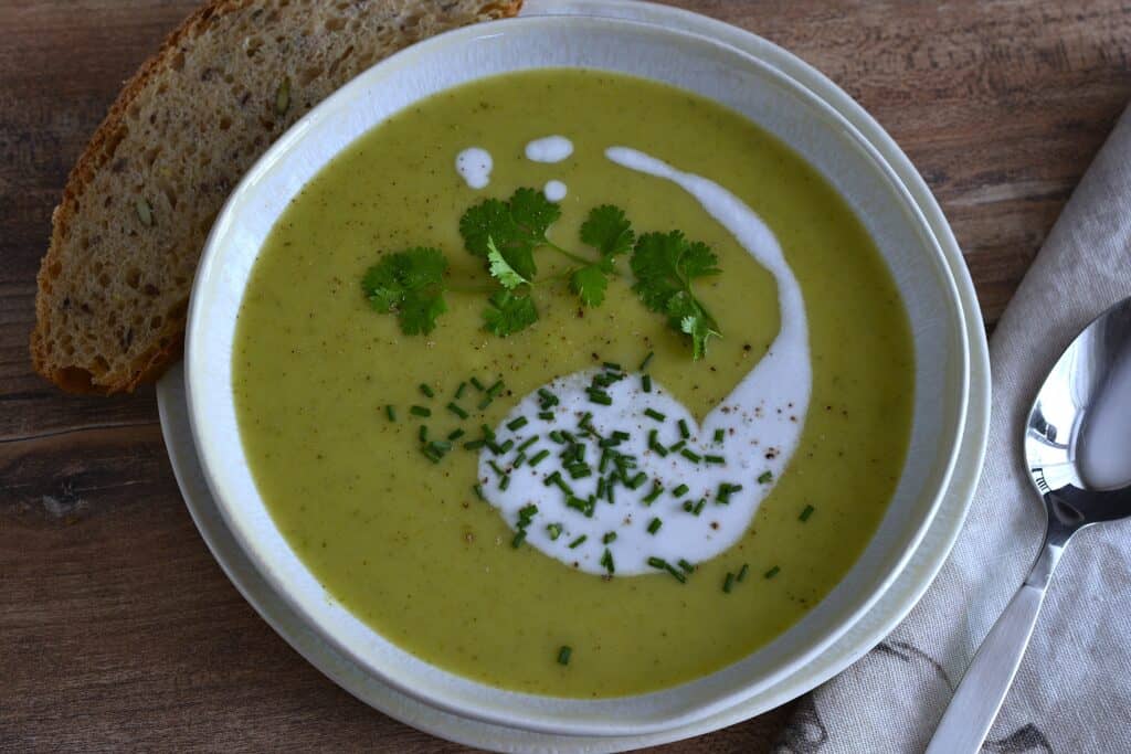 An overhead image of vegan marrow soup with a garnish of coconut milk, green coriander leaf, and chopped chives.