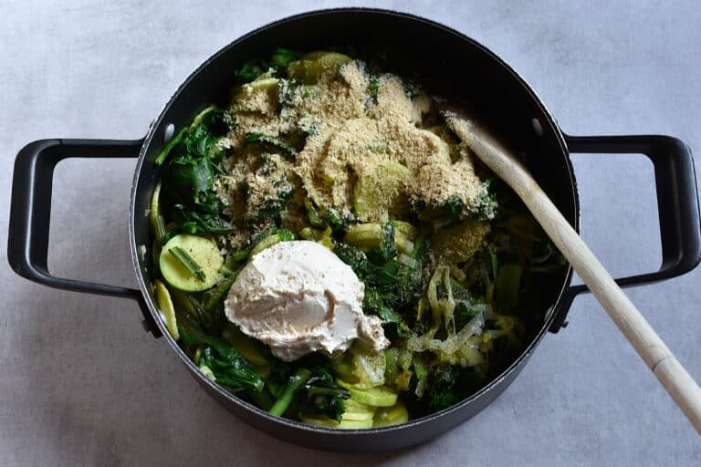 Cooked trombetta, leek and erbette in a saucepan with vegan cashew cream cheese and nutritional yeast flakes.