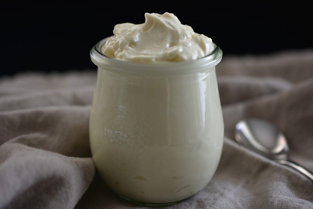 Vegan mayonnaise in a weck glass on a kitchen cloth with a long spoon.