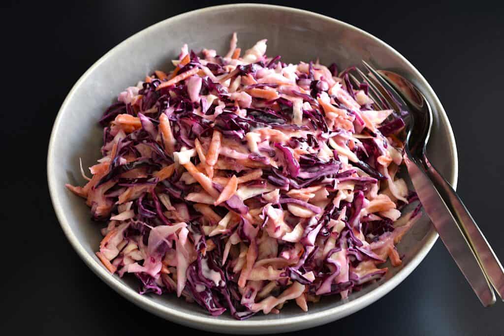 Vegan rainbow coleslaw in a serving bowl with a spoon and fork.