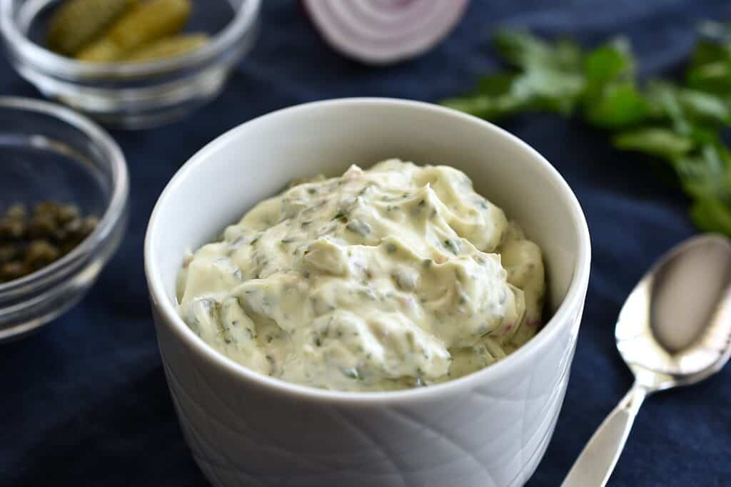 Vegan tartar sauce in a white bowl with a spoon.