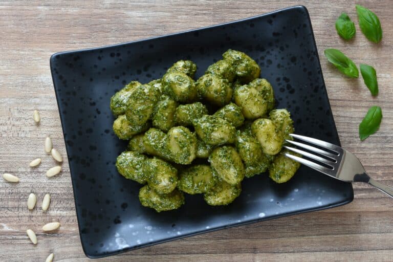 Vegan basil pesto gnocchi on a black plate with a fork.