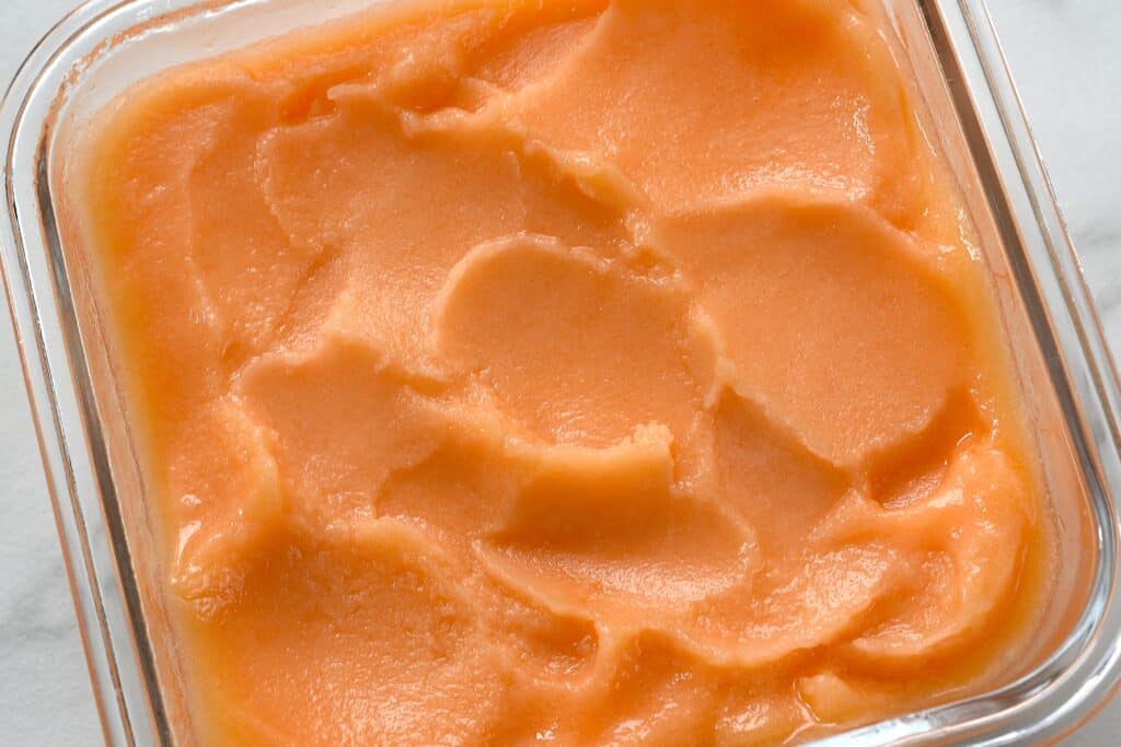 A close-up image of melon sorbet in a freezer container.