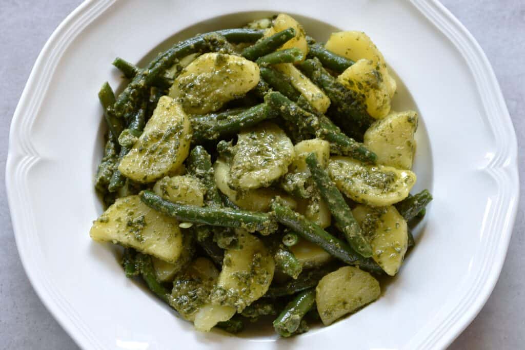 A close-up image of potatoes, green beans and vegan basil pesto on a white plate.