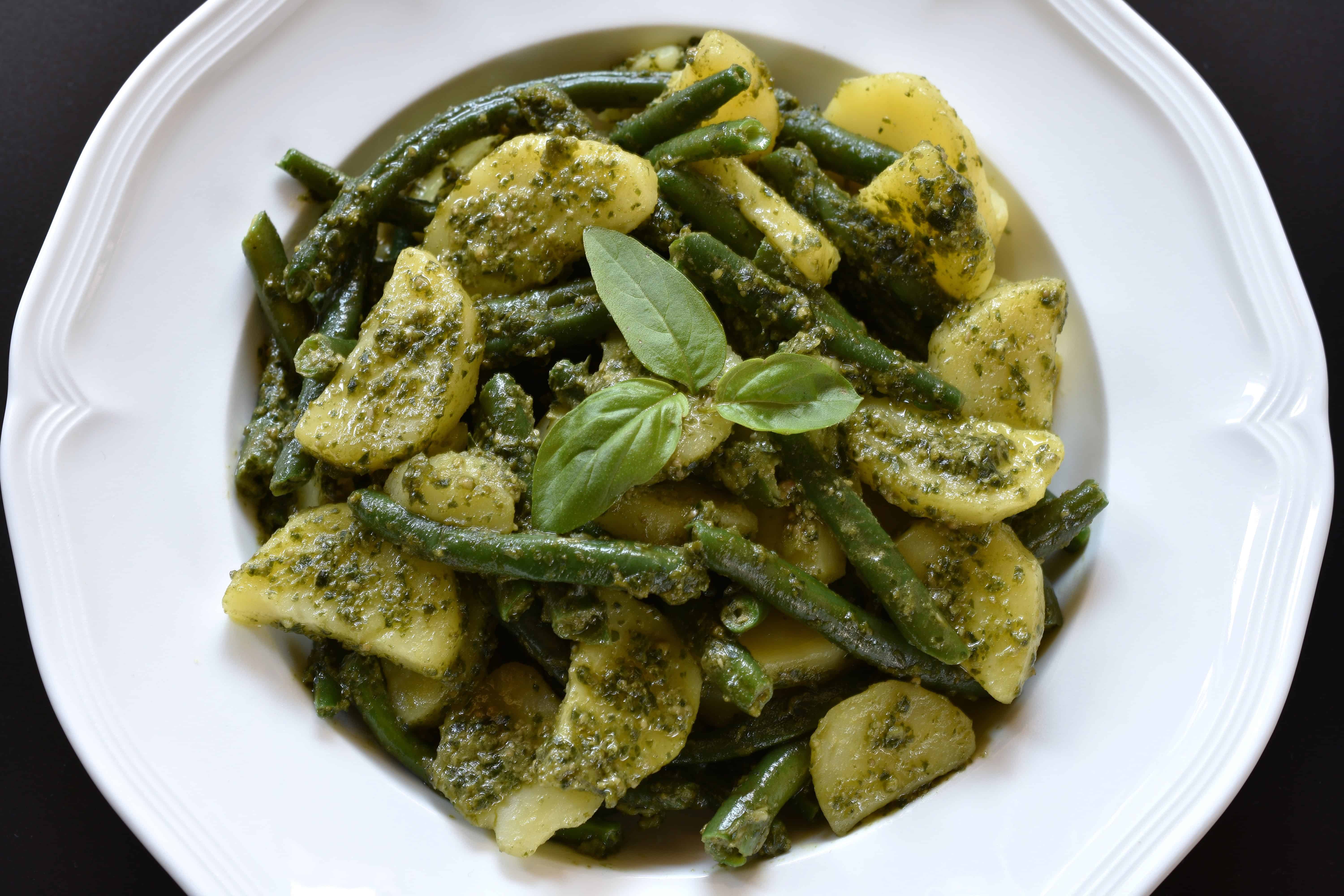 A close-up image of potatoes, green beans and vegan basil pesto on a white plate.