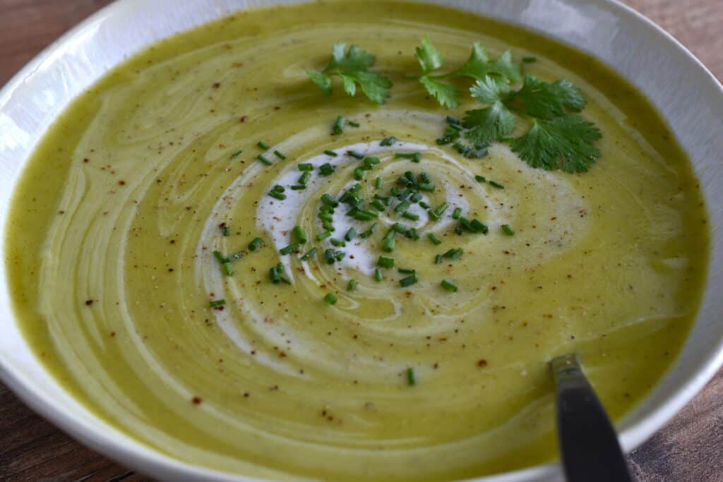 A cllose-up image of vegan marrow soup in a white bowl with a spoon.