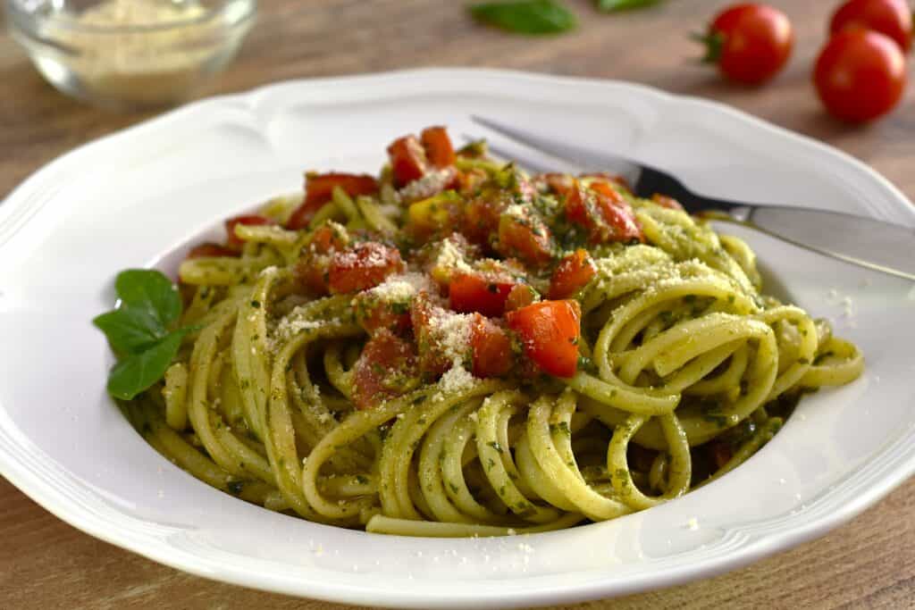 Pesto pasta with cherry tomatoes on a white plate with a fork.