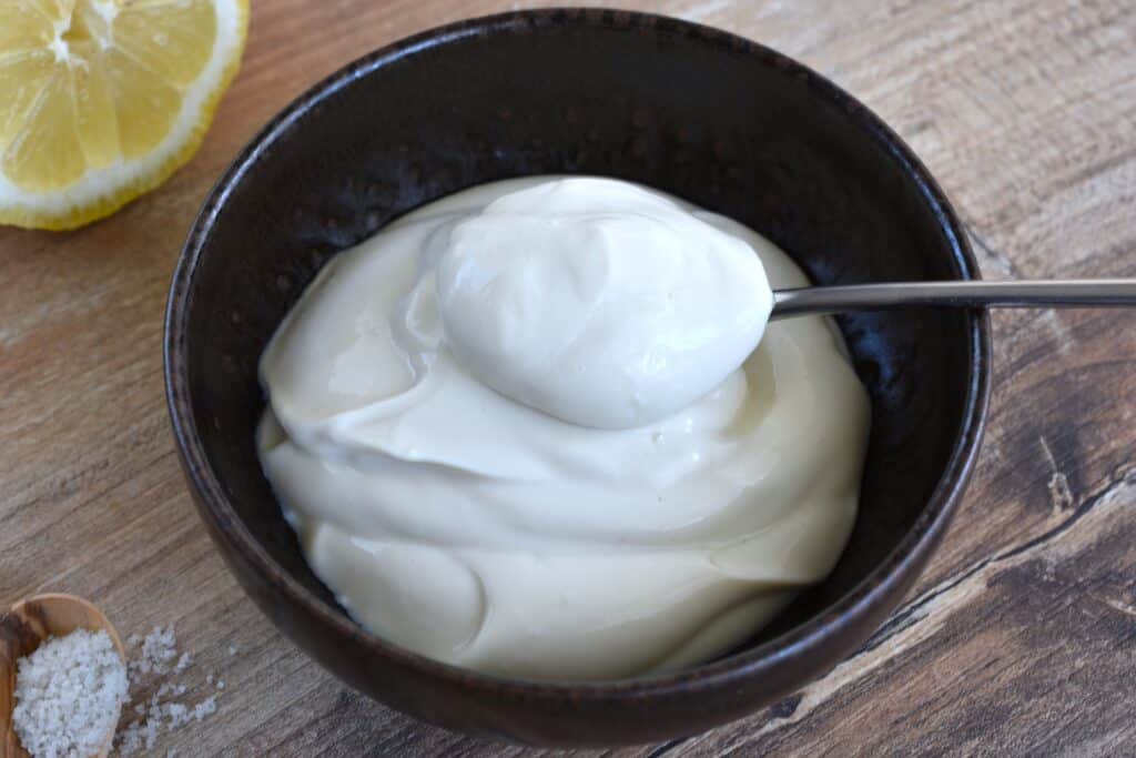 A close-up image of plain vegan yoghurt with a spoon.