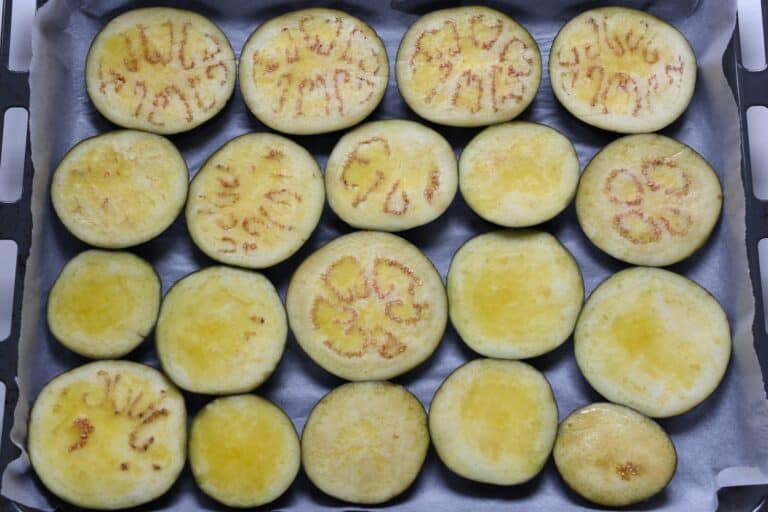 Aubergine (eggplant) slices brushed with oil on parchment paper on an oven tray.