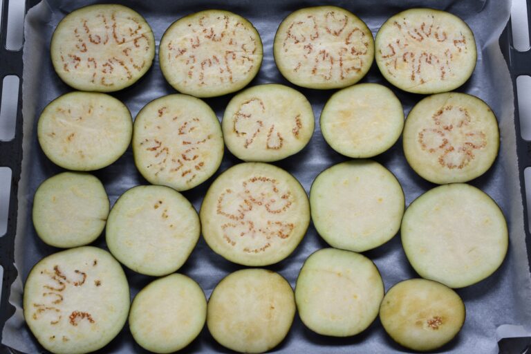 Aubergine (eggplant) slices on parchment paper on an oven tray.