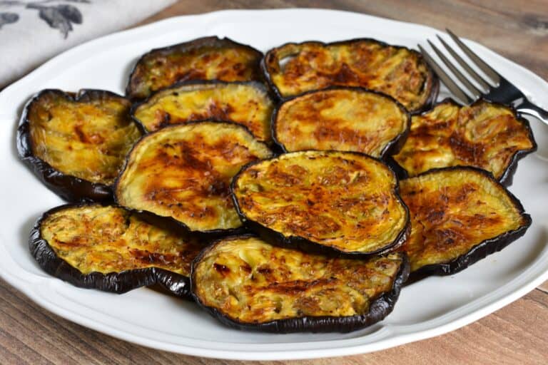 Roasted aubergine (eggplant) slices on a white plate with a fork.