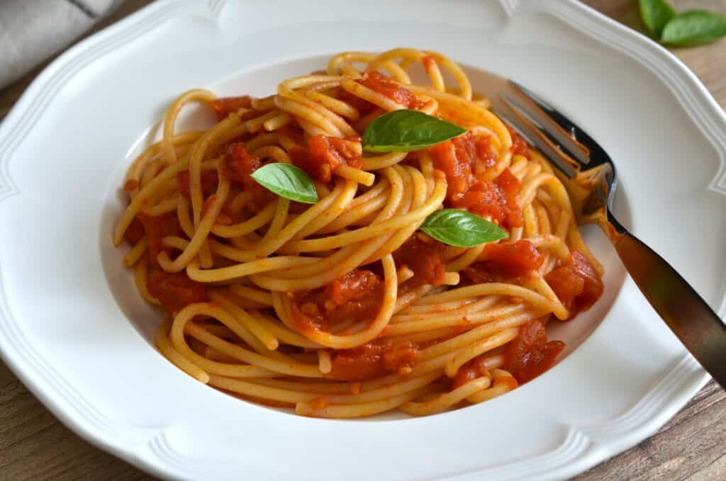 Spaghetti with fresh tomato sauce on a white pasta plate with a fork and a basil leaf garnish.