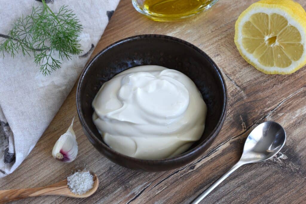 Vegan yoghurt sauce with ingredients and spoons on a table.