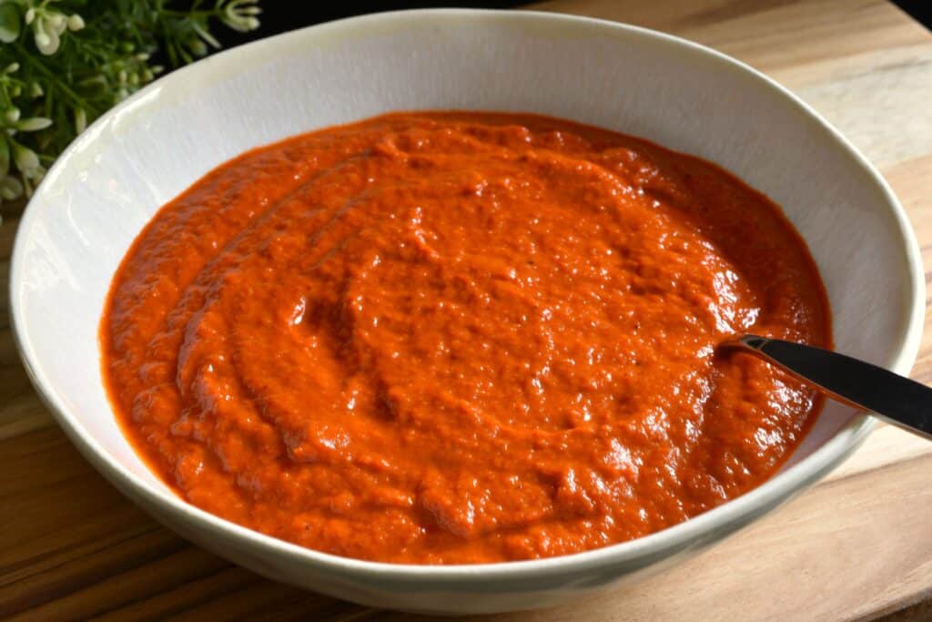 A close-up image of roasted red pepper sauce in a white bowl with a spoon.