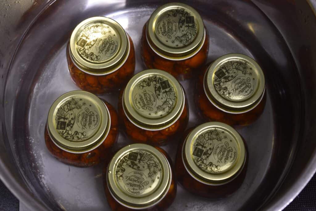 Jars of semi-dried tomatoes in oil in a hot water bath.