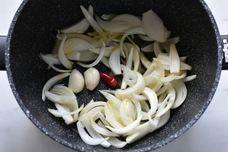 Raw onion, garlic, and a chili pepper in a pan with olive oil.