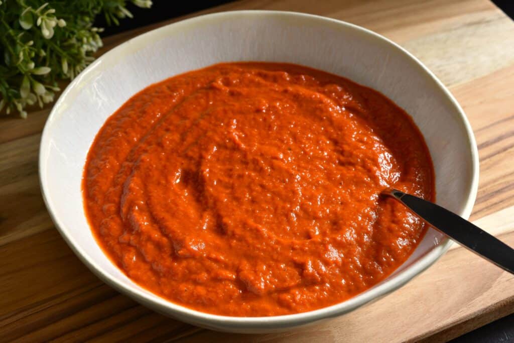 Roasted red pepper sauce in a white bowl with a spoon.