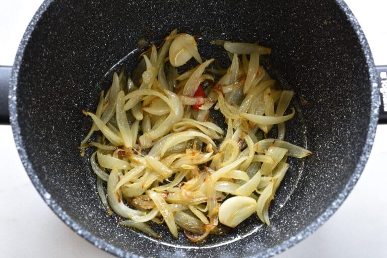 Sautéed onion, garlic, and a chili pepper in a pan.