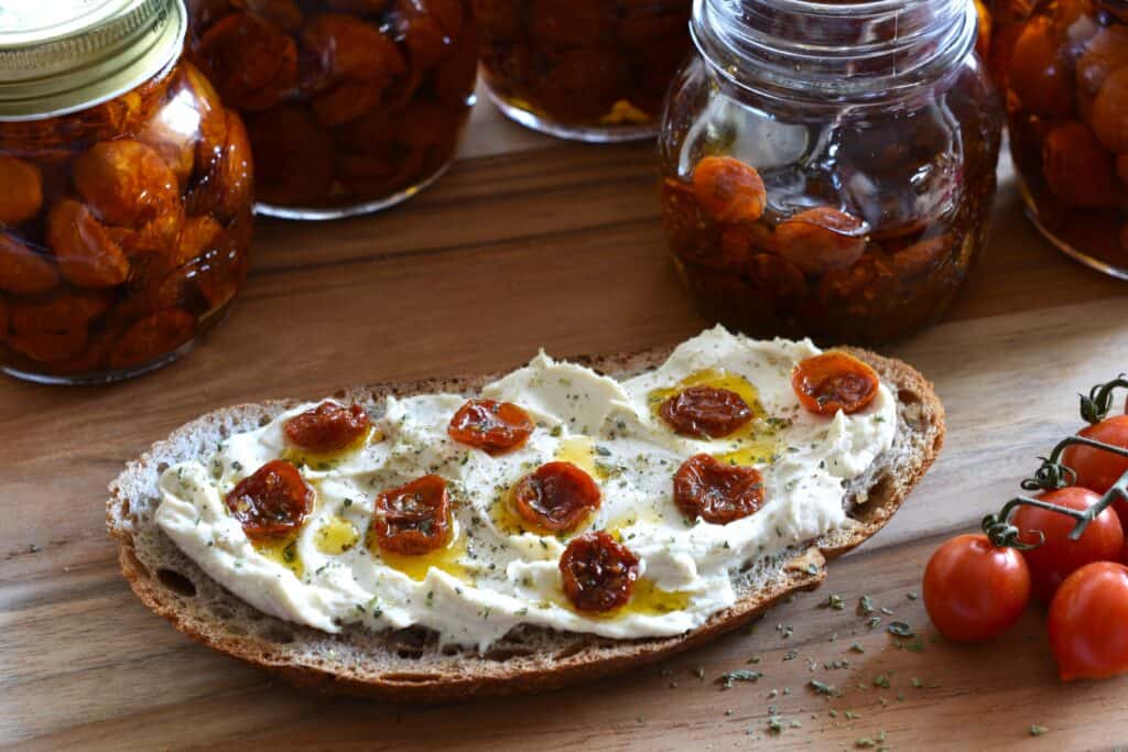 Semi-dried cherry tomatoes in oil on a slice of bread with vegan cheese and oregano.