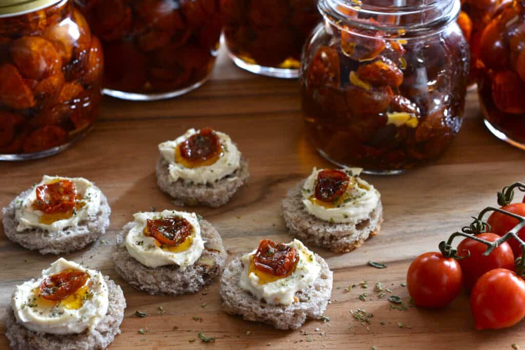 Semi-dried cherry tomatoes in oil on small round pieces of bread with vegan cheese.