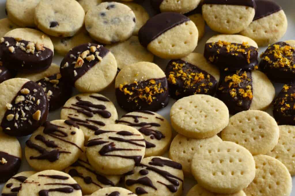 A close-up of festive vegan chocolate-dipped shortbread biscuits with hazelnuts and orange zest.