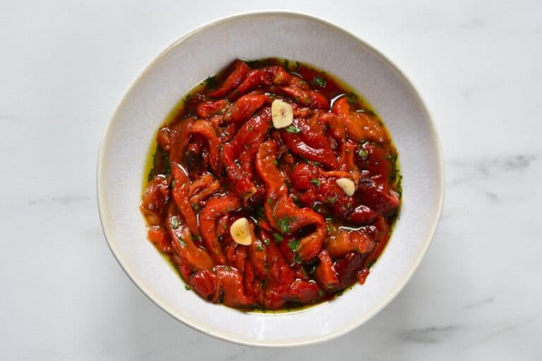 Roasted red pepper strips seasoned with garlic, evo oil, salt, and parsley, in a white bowl.