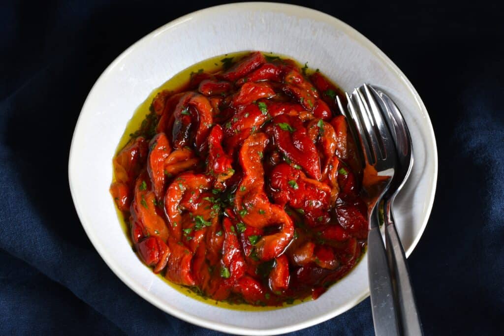 Roasted red pepper strips seasoned with evo oil, sea salt, and parsley, in a white bowl.