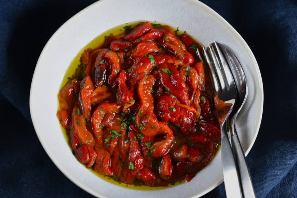 Seasoned roasted red pepper strips in a white bowl with a spoon and fork.