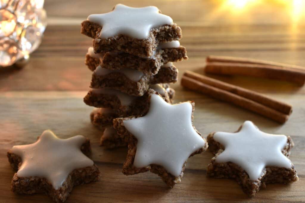 Vegan cinnamon stars (Zimtsterne) on a wooden board with Christmas lighting.